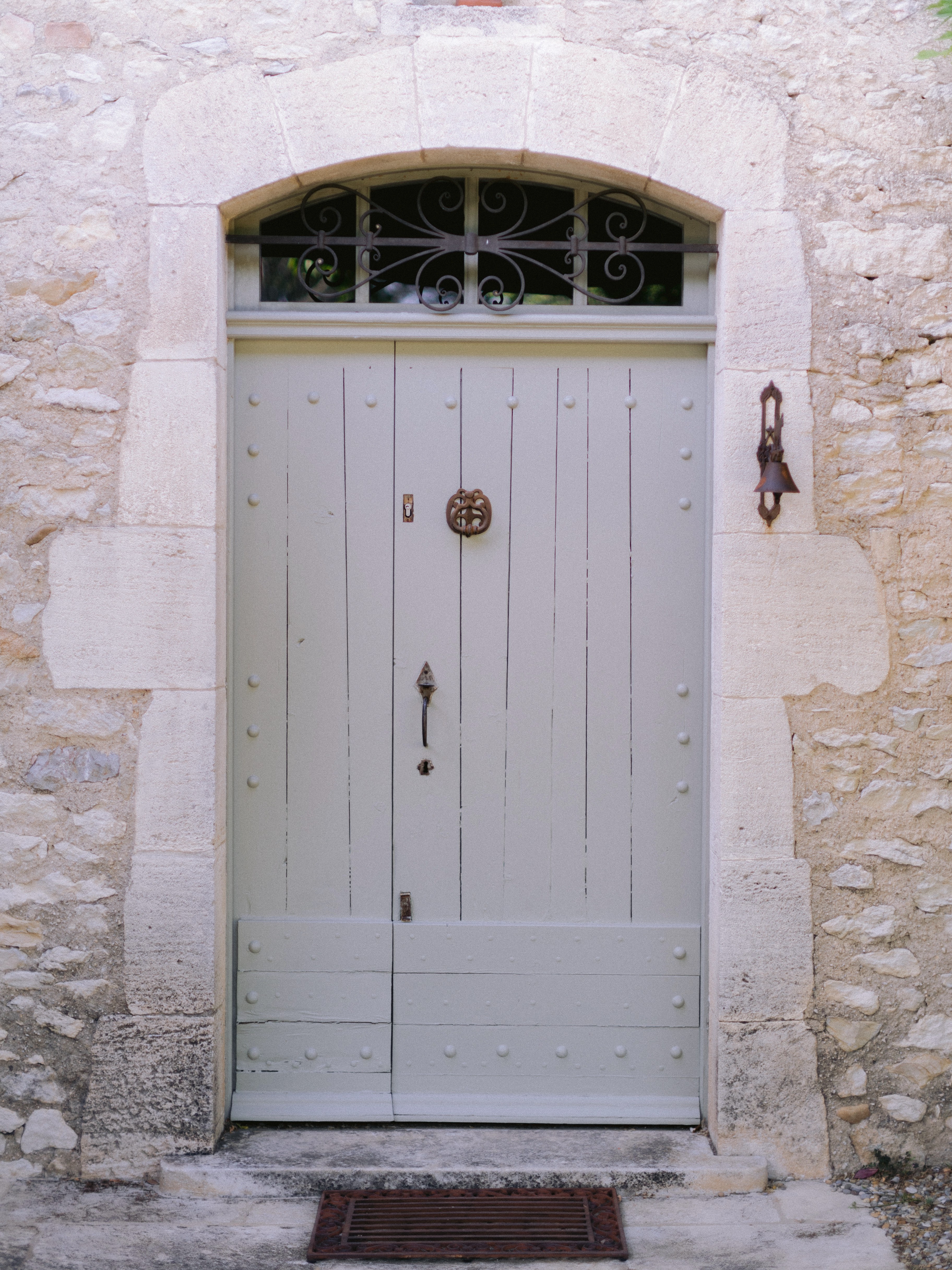 An elegant pale wooden door set in a white stone archway with intricate ironwork and a brass knob, located in a historic building.